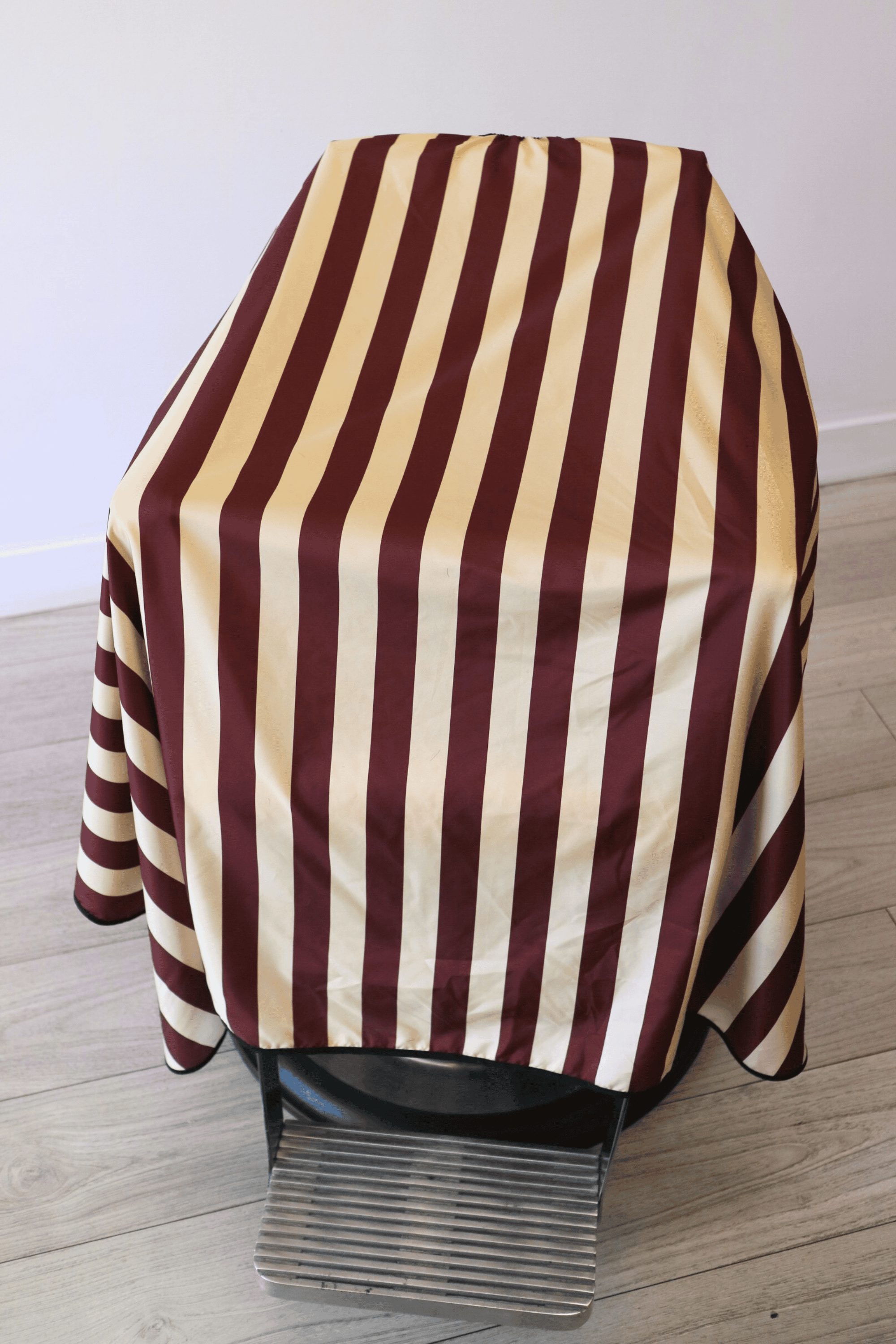 close up photo of burgundy and cream barber cape draped on barber chair