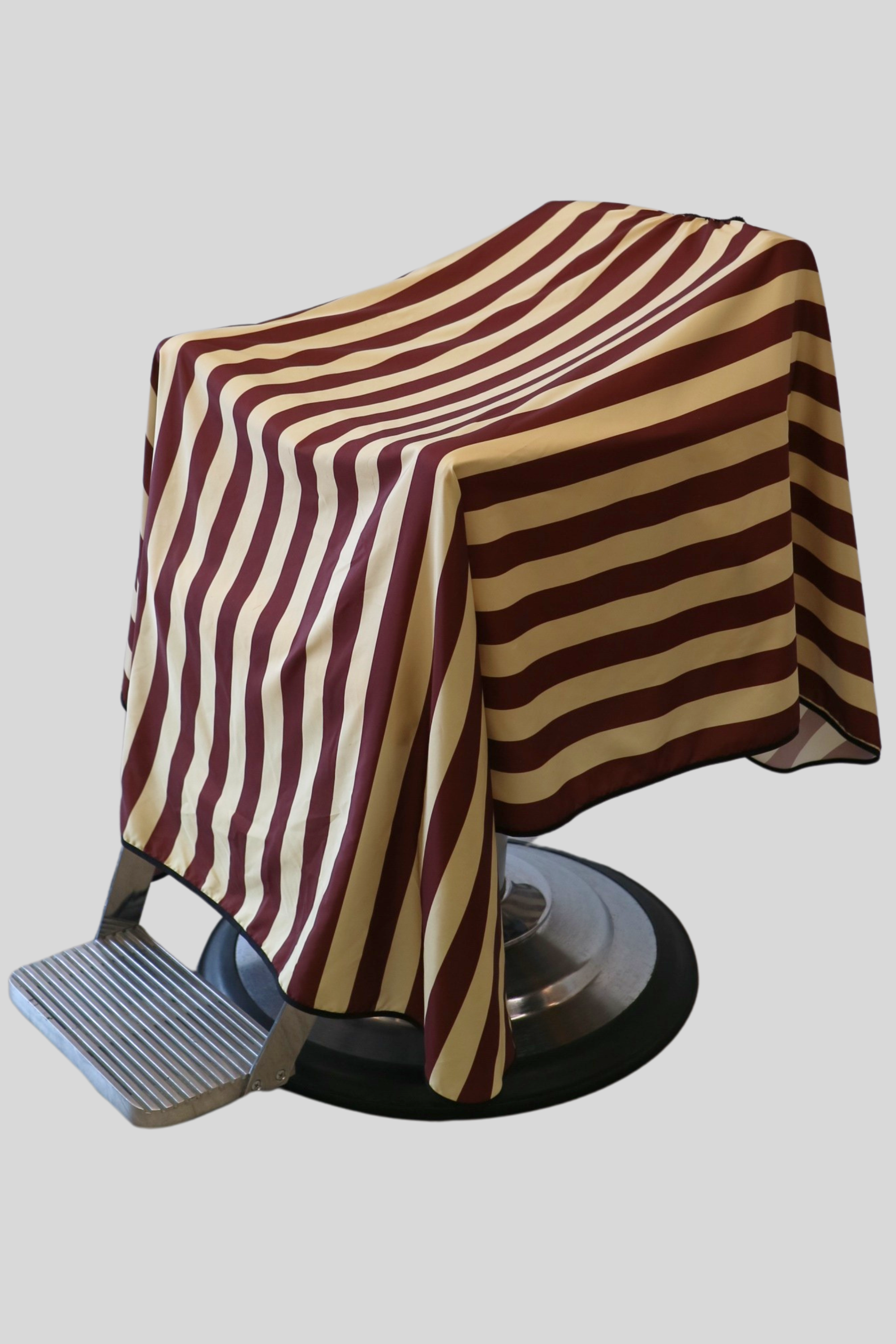 full coverage barber cape that is tan and burgundy striped cape draped on barber chair