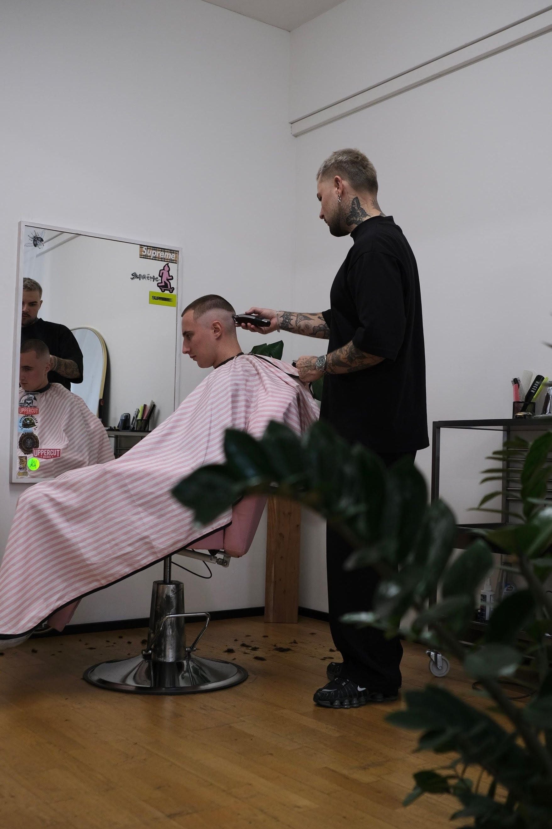 tattooed barber cutting hair using pink street barber cape