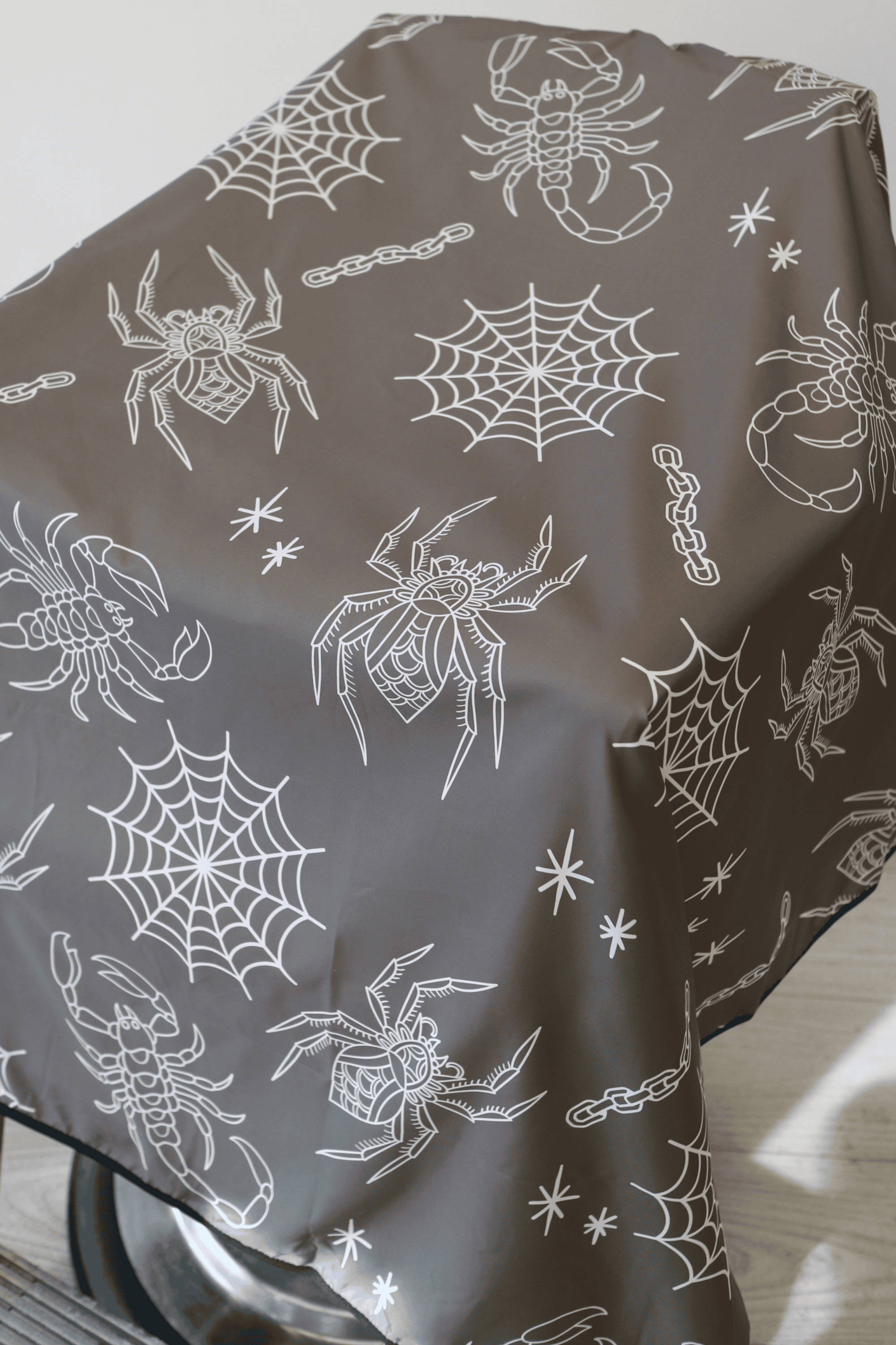 a close up shot of outback barber cape with spiders and web tattoo flash on grey background