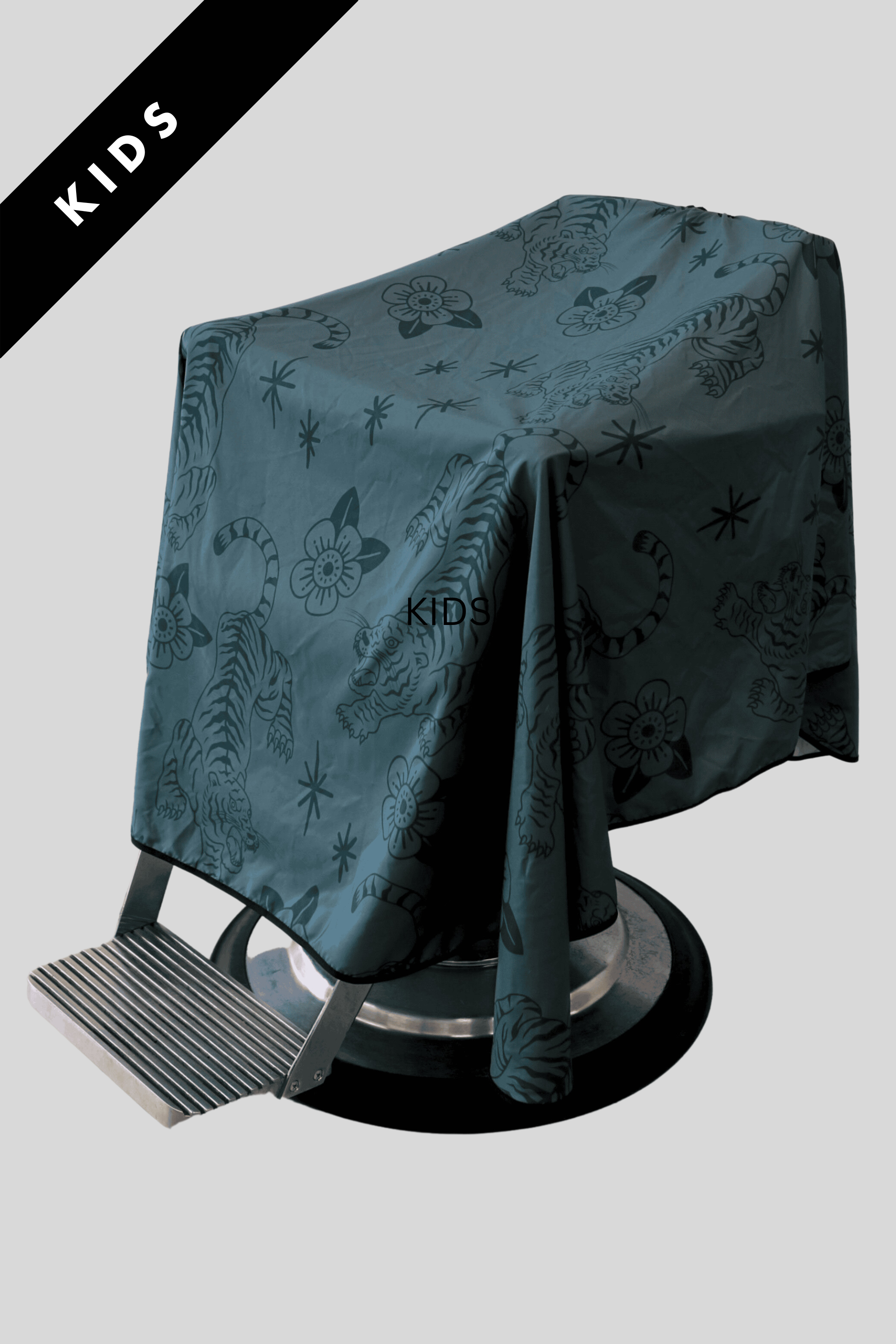 product photo of the Kids Tora Barber cape draped over barbershop chair showcasing the soft green fabric and crawling tiger pattern