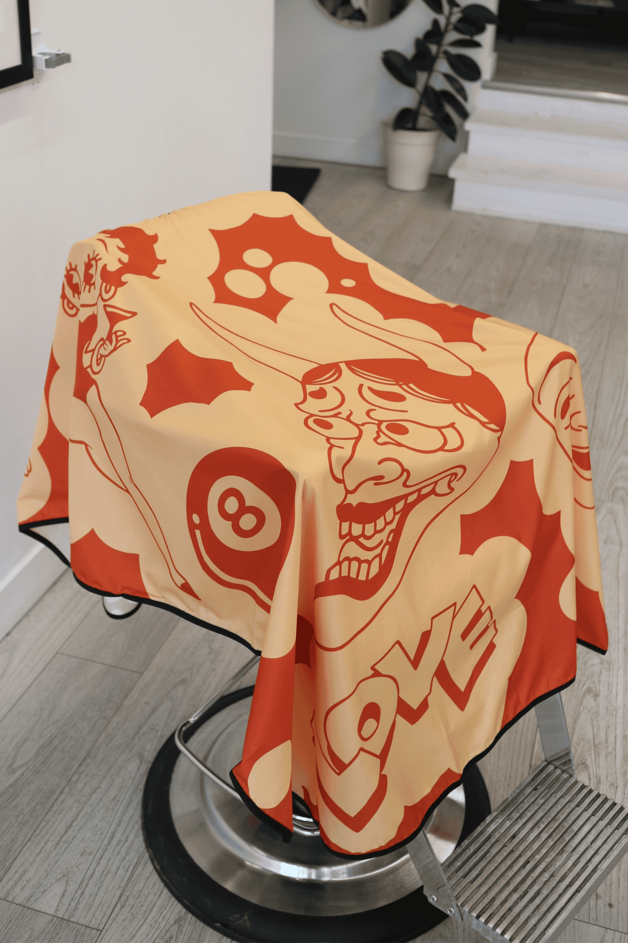 cartoon imagery on a yellow and orange barber cutting cape that is draped on a barber chair