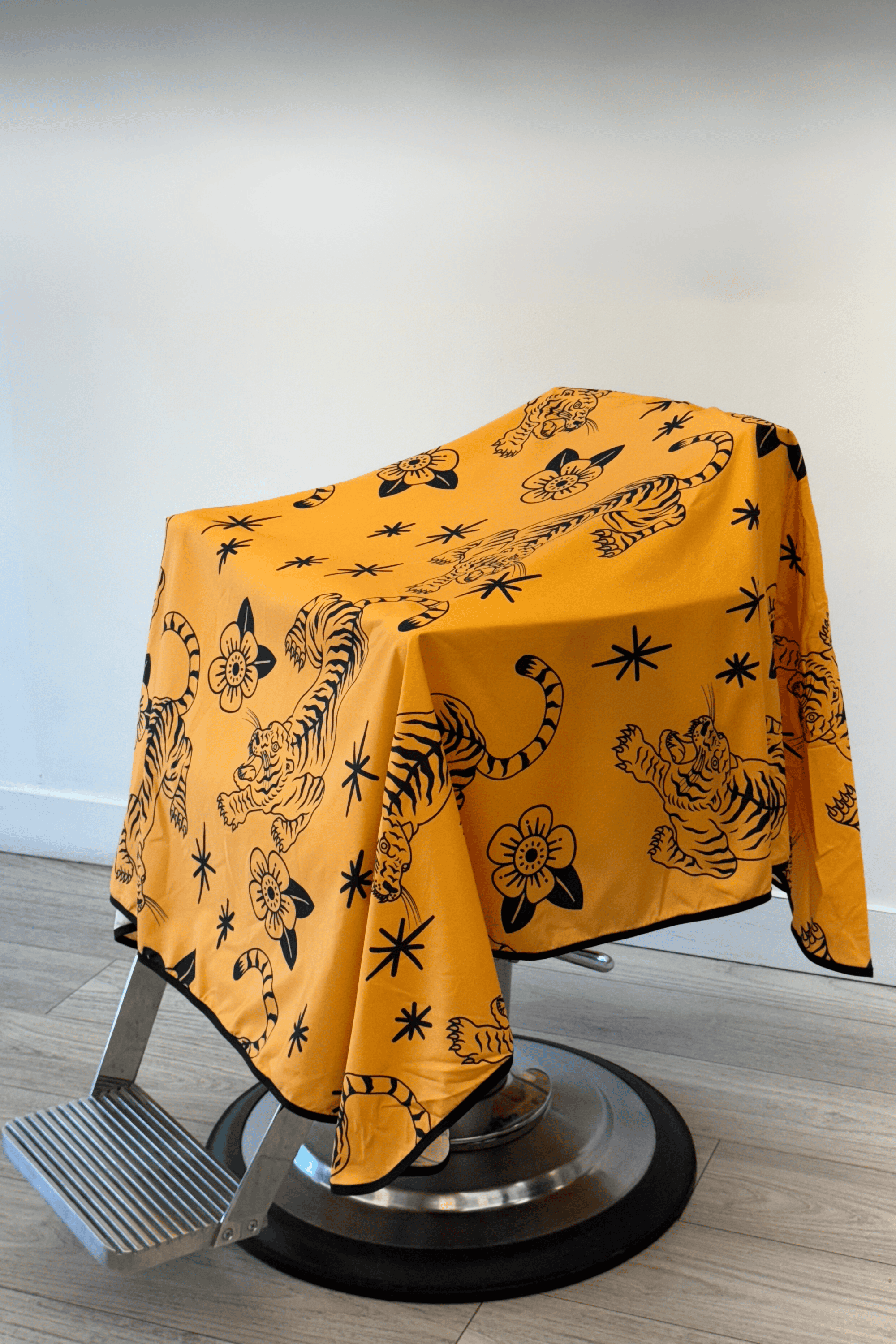 barber cutting cape draped on chair that is yellow with black crawling tigers and flowers