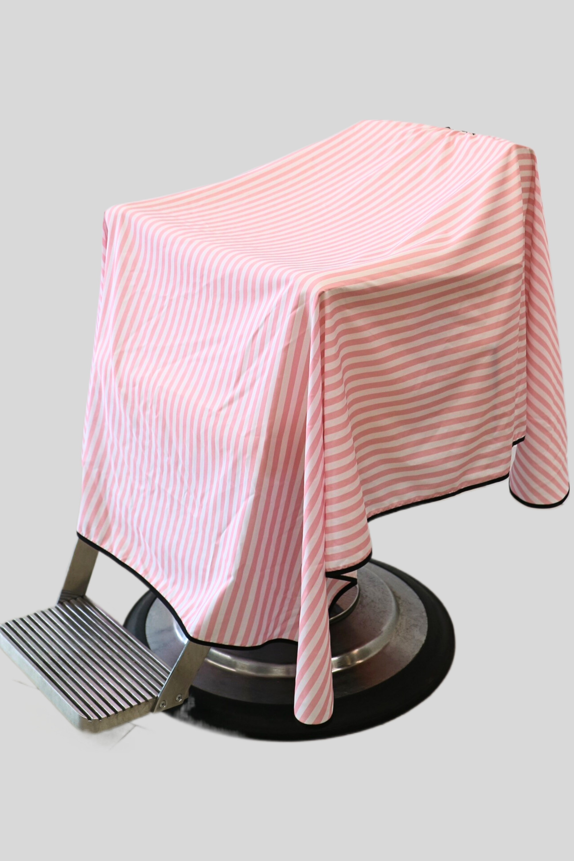 pink and white stripe barber cape on barbershop chair