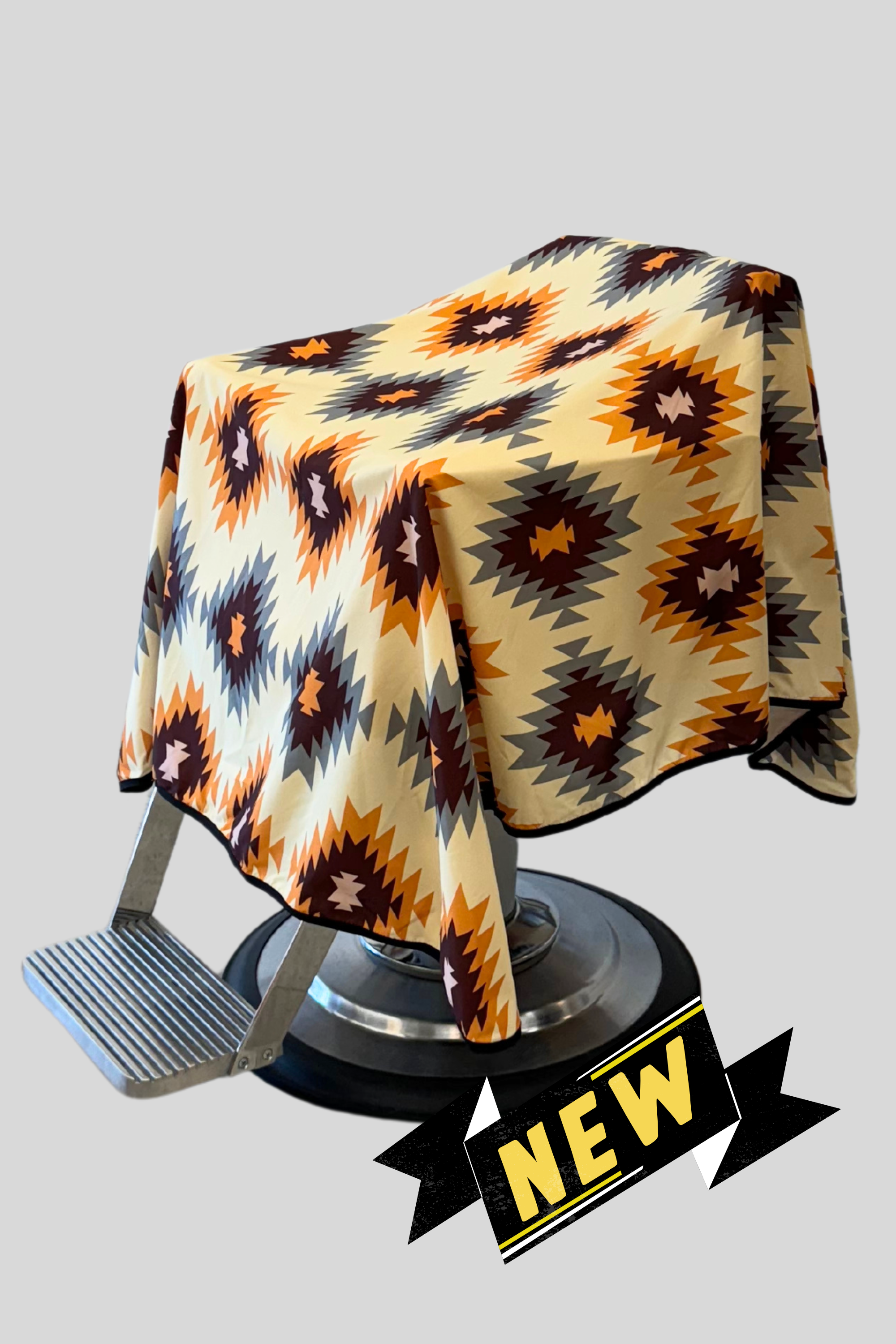 main product photo of the western barber cutting cape draped on barbershop chair.geometric pattern in warm tones